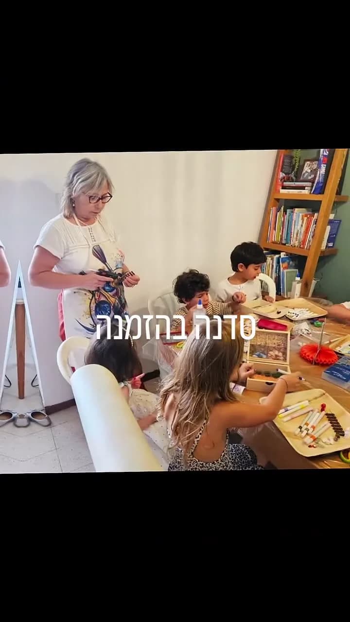 ילדים עובדים סביב שולחן עם מגשים וכלי ציור, ומבוגרת מלווה את הפעילות